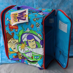 May include: A blue Toy Story locker bag with red trim and a purple handle. The exterior features a repeating pattern of Woody and Buzz Lightyear characters. A white tag attached to the top reads Wiz too! Locker Bag. The interior has a name label.