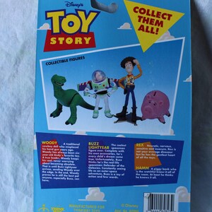 May include: A blue Toy Story collectible figure blister card back featuring illustrations of Rex, Buzz Lightyear, Woody, and Hamm. The packaging includes the Toy Story logo, the text Collect Them All!, and character descriptions for Woody, Buzz, Rex, and Hamm.