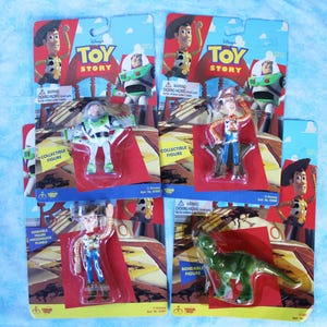 May include: Four Disney Toy Story collectible figures in original blister packaging. The set includes two Woody figures, one Buzz Lightyear figure, and one green dinosaur figure. Each card features character artwork and the Toy Story logo.