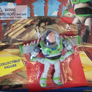 May include: A Buzz Lightyear collectible figure in a white, green, and purple space suit with a clear helmet dome, packaged in a blister card featuring the text WARNING: CHOKING HAZARD-Small parts. Not for children under 3 years and COLLECTIBLE FIGURE.