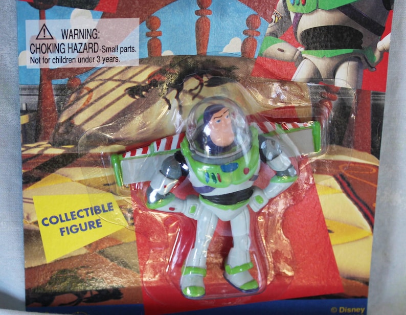 May include: A Buzz Lightyear collectible figure in a white, green, and purple space suit with a clear helmet dome, packaged in a blister card featuring the text WARNING: CHOKING HAZARD-Small parts. Not for children under 3 years and COLLECTIBLE FIGURE.