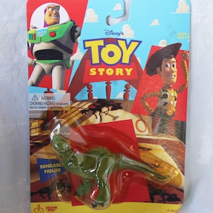 May include: A green bendable dinosaur figure in original packaging featuring Buzz Lightyear and Woody from Disney's Toy Story. The cardboard backing displays the Toy Story logo, a warning label for small parts, and the Think Way brand logo.
