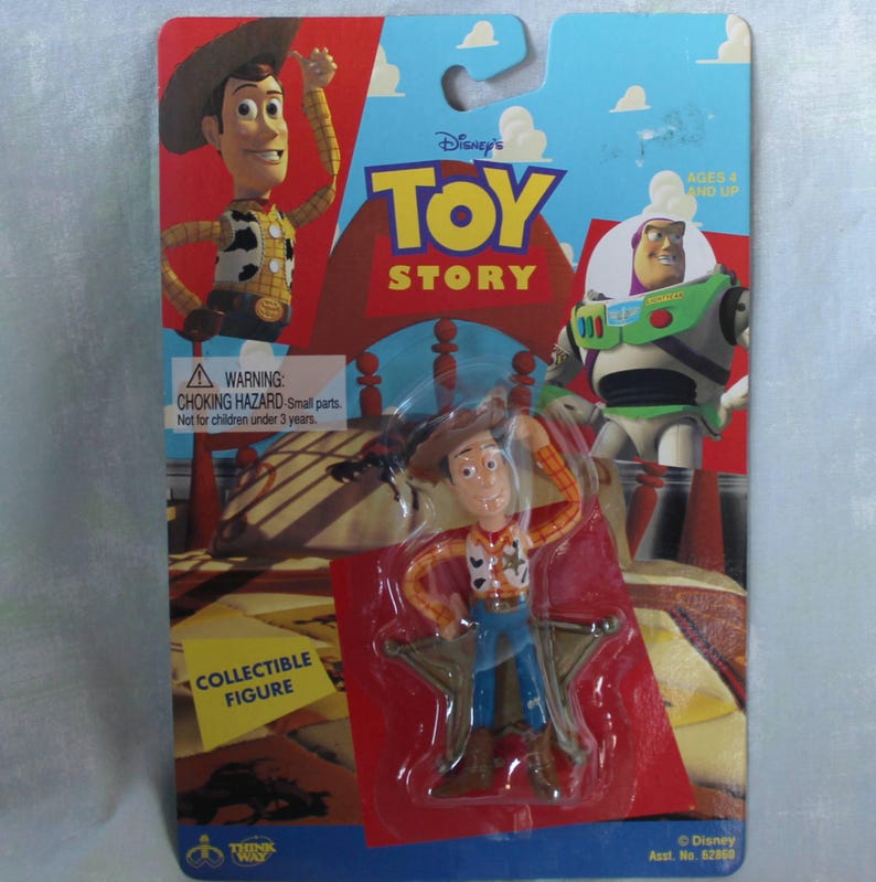 May include: A Toy Story collectible figure of Woody in original blister packaging. The card features Woody and Buzz Lightyear graphics, the Toy Story logo, and a warning label. The plastic-encased figure depicts the cowboy character in a yellow shirt, cow-print vest, blue pants, and brown hat.