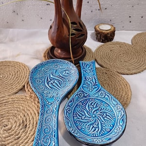 Pode incluir: Dois apoios de colher de cerâmica azul com intrincados desenhos florais. Os apoios de colher estão sobre um tapete de corda trançada.