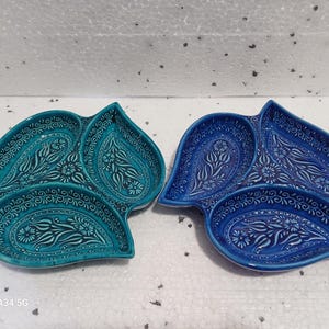 May include: Two ceramic serving dishes, each with three sections. The dishes are shaped like leaves and feature intricate floral patterns. One dish is blue and the other is teal.