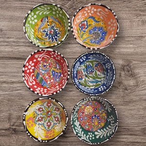 Peut inclure: Six bols en céramique colorés avec des motifs floraux. Les bols ont un fond blanc avec des motifs floraux bleus, rouges, verts et jaunes.