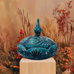 May include: A teal blue ceramic lidded box with intricate floral designs. The box has a rounded shape and a decorative knob on the lid.