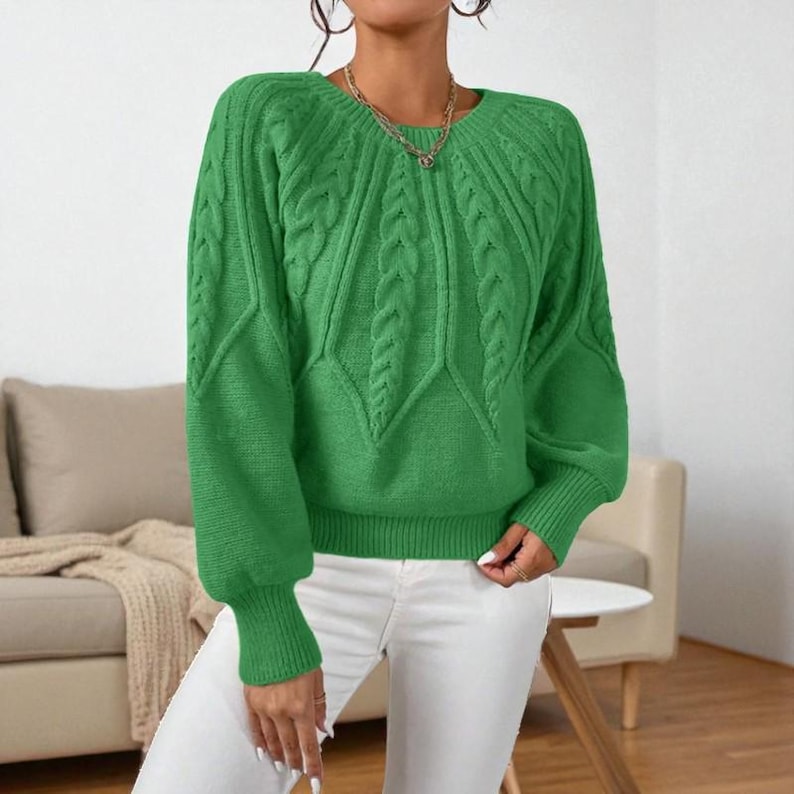 May include: A bright green cable-knit sweater with long sleeves and a crew neck. The sweater features a textured pattern on the front and sleeves. The cuffs and hem are ribbed. The model is wearing white pants.
