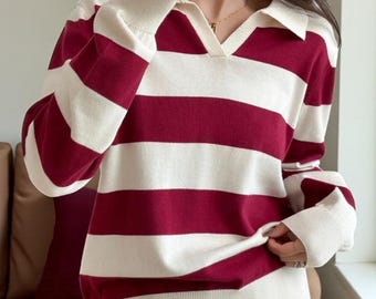 May include: A long-sleeved sweater with a rugby-style design. The sweater features wide horizontal stripes in burgundy and white. It has a collared neckline and ribbed cuffs and hem. The sleeves are long and the fit appears relaxed.