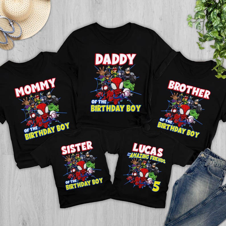 May include: A set of five black t-shirts featuring a graphic print of various superhero characters on a spider web background. The shirts include text labels such as DADDY OF THE BIRTHDAY BOY, MOMMY OF THE BIRTHDAY BOY, BROTHER OF THE BIRTHDAY BOY, SISTER OF THE BIRTHDAY BOY, and LUCAS AND THE AMAZING FRIENDS 5.