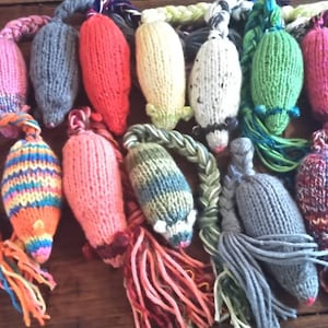 May include: A collection of colorful, hand-knitted cat toys shaped like mice. Each toy features a different color scheme, including pink, gray, red, yellow, and green. Braided yarn tails and yarn tassels add texture and visual interest to these playful pet accessories.