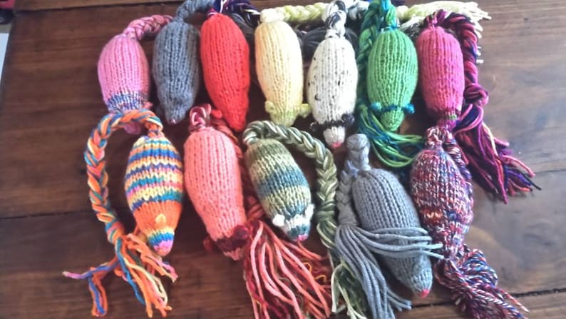 May include: A collection of colorful, hand-knitted cat toys shaped like mice. Each toy features a different color scheme, including pink, gray, red, yellow, and green. Braided yarn tails and yarn tassels add texture and visual interest to these playful pet accessories.