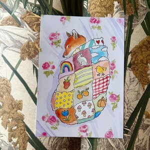 May include: A rectangular art print featuring a watercolour illustration of a fox sleeping under a patchwork quilt. The quilt is composed of various squares displaying motifs including a rainbow, a rabbit, a chick, a strawberry, mushrooms, and a pumpkin.
