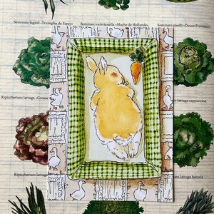 May include: A rectangular card featuring a watercolour illustration of a sleeping yellow rabbit on a green and white checkered blanket. The rabbit is positioned next to a small orange carrot. The border is decorated with white ducks.