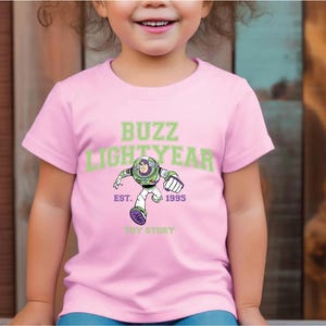 a young girl wearing a pink buzz lightyear t - shirt