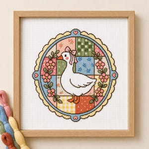 May include: A framed cross-stitch embroidery featuring a white goose with a pink bow, centred within a circular scalloped border. The background consists of a colourful patchwork grid of floral, polka dot, and checkered patterns in pastel tones.