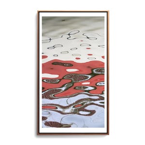 Puede incluir: Impresión artística abstracta que muestra reflejos de agua. La obra presenta una mezcla de colores rojo, blanco y gris con formas y patrones orgánicos. La imagen está enmarcada en un marco de madera marrón fino.