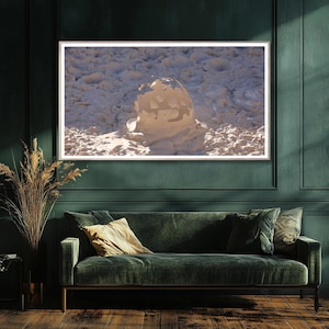May include: A framed photograph of a natural landscape. The image features a light-colored, textured formation in the center, set against a backdrop of similar textures. The photograph is displayed above a green velvet sofa.