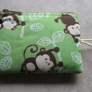 May include: A green zippered pouch with a brown monkey design. The pouch has a white strap and a white background with green leaves.