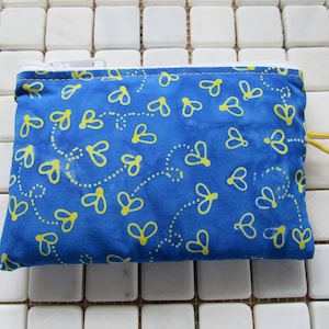 May include: A small blue zippered pouch with a white zipper and a yellow and blue pattern of flying bees. The pouch is lying on a white tiled surface.
