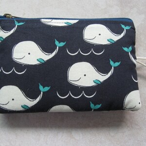 May include: A dark blue zippered pouch with a white whale pattern and teal fins. The pouch has a white cotton drawstring.