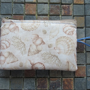 May include: A beige zippered pouch with a blue zipper pull and a blue fabric loop. The pouch has a seashell pattern printed on it.