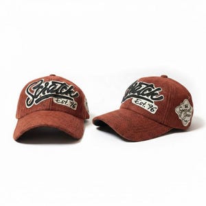 Op de afbeelding: Twee roestkleurige baseballpetten met gebogen kleppen worden getoond tegen een witte achtergrond. De petten hebben het woord "Scratch" in een cursief lettertype, met "Est. '96" eronder. Eén pet heeft een patch met "Special Jean".