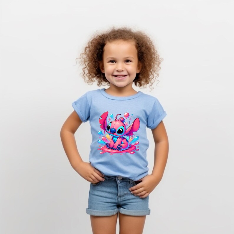 May include: A young girl wearing a light blue t-shirt with a pink Stitch character graphic. The graphic shows Stitch sitting in a puddle of pink and blue paint with blue and pink paint splatters around him.