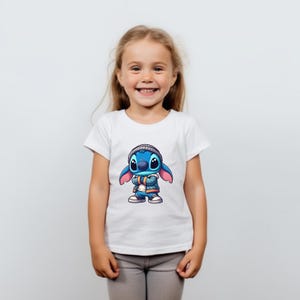 May include: A white t-shirt with a blue cartoon character wearing a blue jacket and a beanie. The character has large blue eyes and a pink nose.