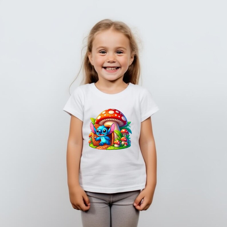 May include: A white t-shirt with a blue cartoon character standing in front of a red and white mushroom house. The character has blue ears and is holding a red object. There are smaller mushrooms in the background.