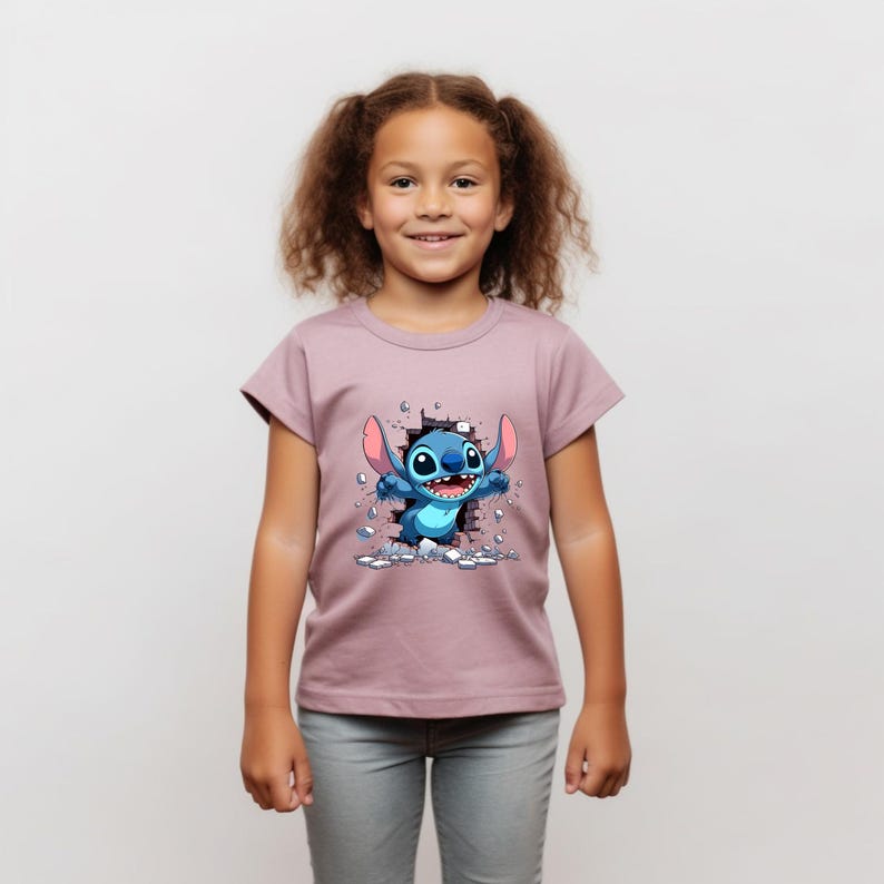 K&ouml;nnte beinhalten: Ein junges M&auml;dchen tr&auml;gt ein mauvefarbenes T-Shirt mit einem Cartoon-Bild von Stitch, der eine Ziegelmauer durchbricht. Stitch ist blau mit gro&szlig;en Ohren und einem verschmitzten Grinsen.