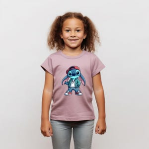 May include: A young girl wearing a mauve t-shirt with a blue cartoon character wearing a red hat, green jacket, and jeans. The character is holding a microphone and has a silver chain around its neck.