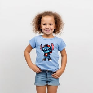May include: A young child wearing a light blue t-shirt with a cartoon image of Stitch wearing a red hat and a denim jacket. The child is smiling and has curly brown hair.