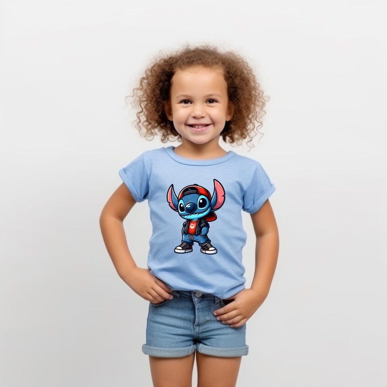 May include: A young child wearing a light blue t-shirt with a cartoon image of Stitch wearing a red hat and a denim jacket. The child is smiling and has curly brown hair.