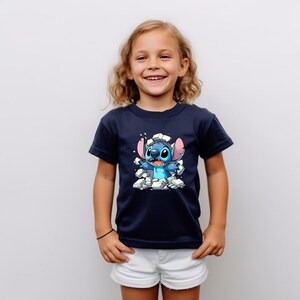 K&ouml;nnte beinhalten: Ein junges Kind tr&auml;gt ein marineblaues T-Shirt mit einem Cartoon-Bild von Stitch, der eine Wand durchbricht. Stitch ist blau mit wei&szlig;en Augen und einer rosa Nase.