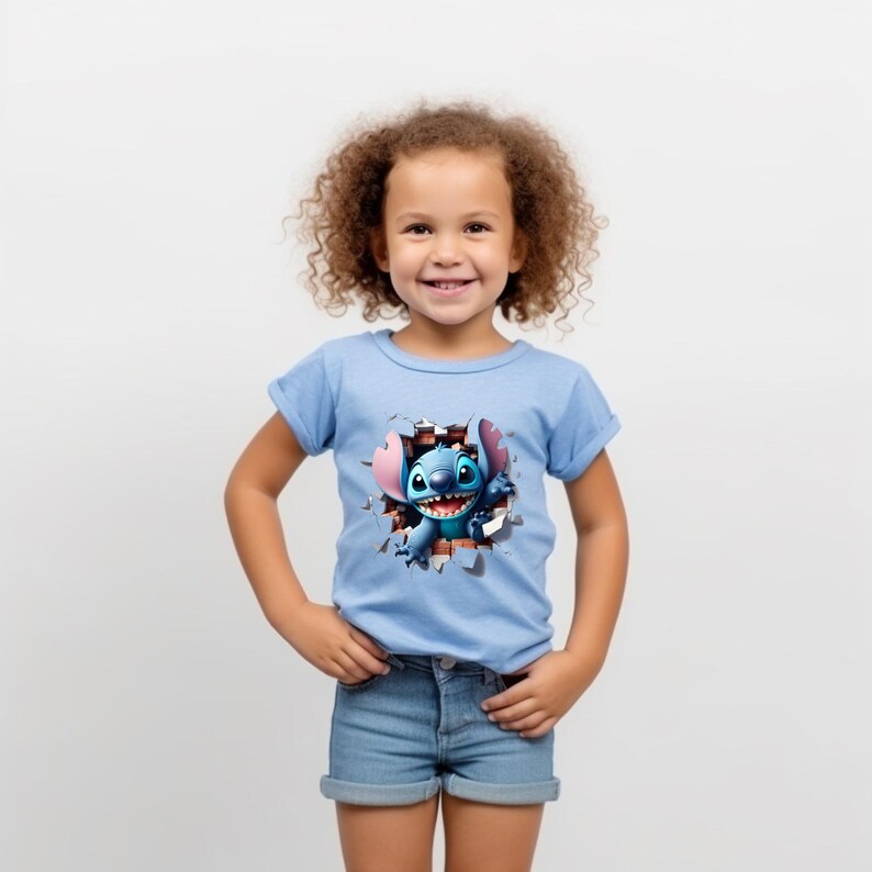 K&ouml;nnte beinhalten: Ein junges M&auml;dchen tr&auml;gt ein hellblaues T-Shirt mit einem Cartoon-Stitch-Charakter, der durch den Stoff bricht. Der Charakter ist blau mit rosa Ohren und l&auml;chelt. Das M&auml;dchen tr&auml;gt Jeans-Shorts und hat lockiges braunes Haar.