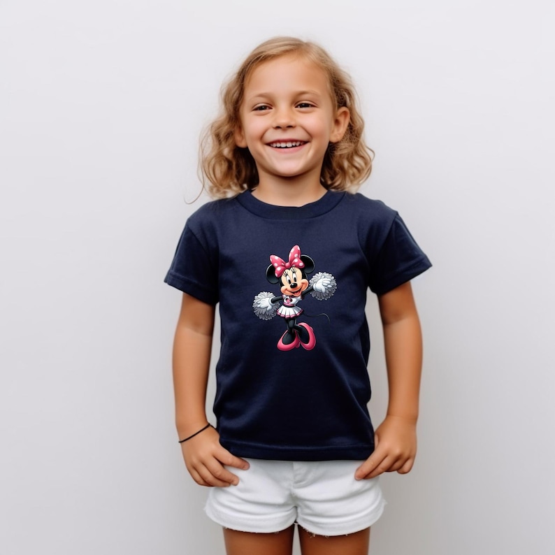 May include: A young girl wearing a navy blue t-shirt with a graphic of Minnie Mouse dressed as a cheerleader. The graphic features Minnie Mouse in a pink and white cheerleader outfit with pom-poms.