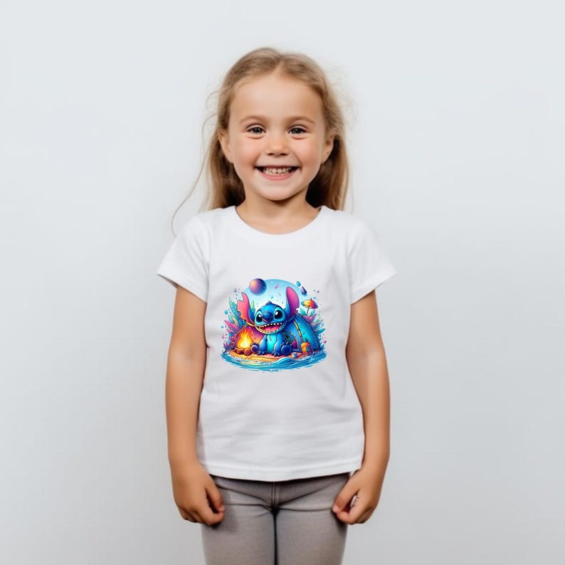 Puede incluir: Una camiseta blanca con un gr&aacute;fico colorido de un personaje de dibujos animados azul con orejas grandes, sentado en una playa con una fogata. El personaje est&aacute; rodeado de detalles vibrantes y caprichosos. La camiseta la lleva una ni&ntilde;a.