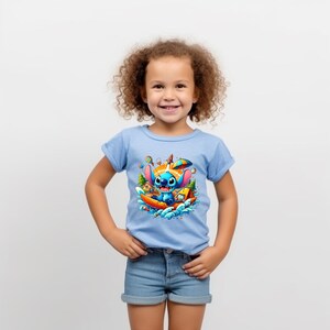 Puede incluir: Una camiseta azul claro con un gr&aacute;fico colorido de Stitch de Lilo & Stitch en un bote. El personaje de dibujos animados est&aacute; rodeado de agua, &aacute;rboles y un campamento. La camiseta la lleva un ni&ntilde;o peque&ntilde;o.