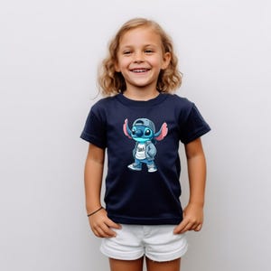May include: A navy blue t-shirt with a cartoon image of Stitch wearing a blue baseball cap, a white shirt with the word "Stitch" on it, a blue jacket, and blue jeans.