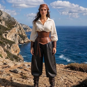 May include: A cream-colored long-sleeved shirt with a collar, a brown leather corset with a belt, dark charcoal loose-fitting trousers, brown leather wrist cuffs, a brown headscarf, and dark brown boots with buckles and straps.