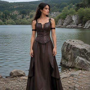 May include: A dark brown floor-length dress featuring a fitted bodice with a lace-up front closure, thin shoulder straps, and arm bands. The skirt has a high-waisted design with side slits that reveal a layered fabric construction.