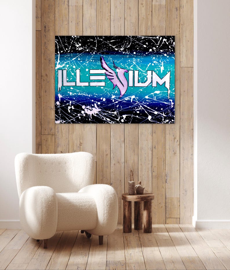 Op de afbeelding: Een ingelijst kunstwerk met het woord "ILLENIUM" in witte letters, een roze vleugelontwerp en een achtergrond van blauwe en zwarte verfspetters. Het kunstwerk hangt aan een houten muur boven een witte fauteuil.