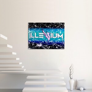Op de afbeelding: Een canvas kunstwerk met het woord "ILLENIUM" in witte blokletters, een paars vleugelontwerp en een blauw-zwarte achtergrond met witte verfspatten. Het kunstwerk wordt aan een witte muur getoond.