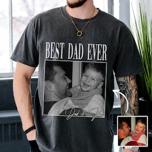 Puede incluir: Camiseta gris oscuro con el texto "BEST DAD EVER" sobre una foto en blanco y negro de un padre y un niño. La foto está enmarcada con un borde blanco, y los nombres "Dad & John" están escritos debajo.