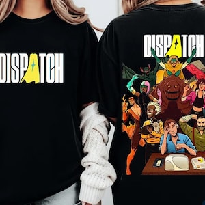 May include: Black t-shirt with the word "DISPATCH" in white block letters and a yellow cape design. The back of the shirt features a colorful comic-style illustration of a group of people, including superheroes and office workers.
