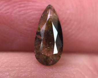 May include: A pear-shaped, faceted gemstone with a brown and amber color gradient. The gem has a pointed top and a wider, rounded base. The facets create a play of light and shadow.