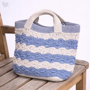 May include: A handmade crochet tote bag with a striped pattern in light blue and off-white. The bag has a sturdy, integrated handle and is sitting on a wooden chair. The bag's design features a textured, wave-like pattern.