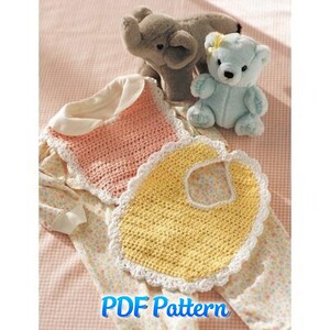 Puede incluir: Dos baberos de bebé de ganchillo, uno rosa y otro amarillo, con bordes festoneados blancos, junto a un elefante gris y un osito de peluche azul. Los baberos están sobre un pelele con estampado floral. El texto "PDF Pattern" es visible.