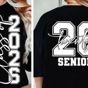 May include: Black long-sleeve shirt with white text. The front of the shirt says "Class of 2026" in a vertical script. The back of the shirt features the number "26" with the word "twenty" and "SENIOR" below.